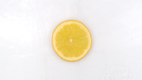 Top-view:-on-a-white-background-a-fresh-orange-is-lying-in-the-water-water-drops-are-falling-from-above-and-splashes-are-falling-in-slow-motion-in-all-directions.